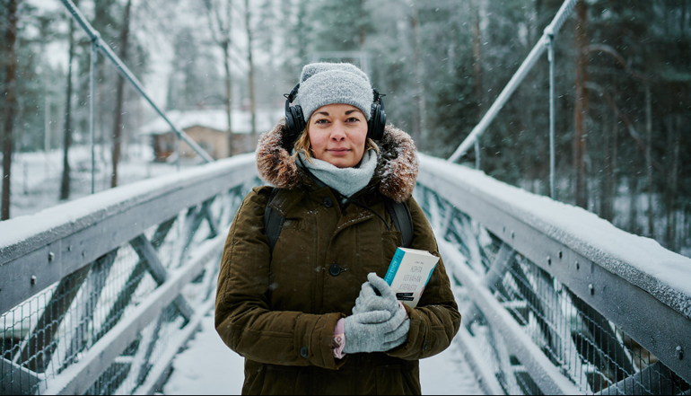 Kirjastojen podcastit. Nainen seisoo talvisessa maisemassa korvillaan kuulokkeet ja sylissä kirjoja. Kuva Ilkka Vuorinen / Kirjastot.fi